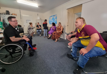 Seven male and female attendees at a Queenslanders with Disability digital workshop sitting and chatting