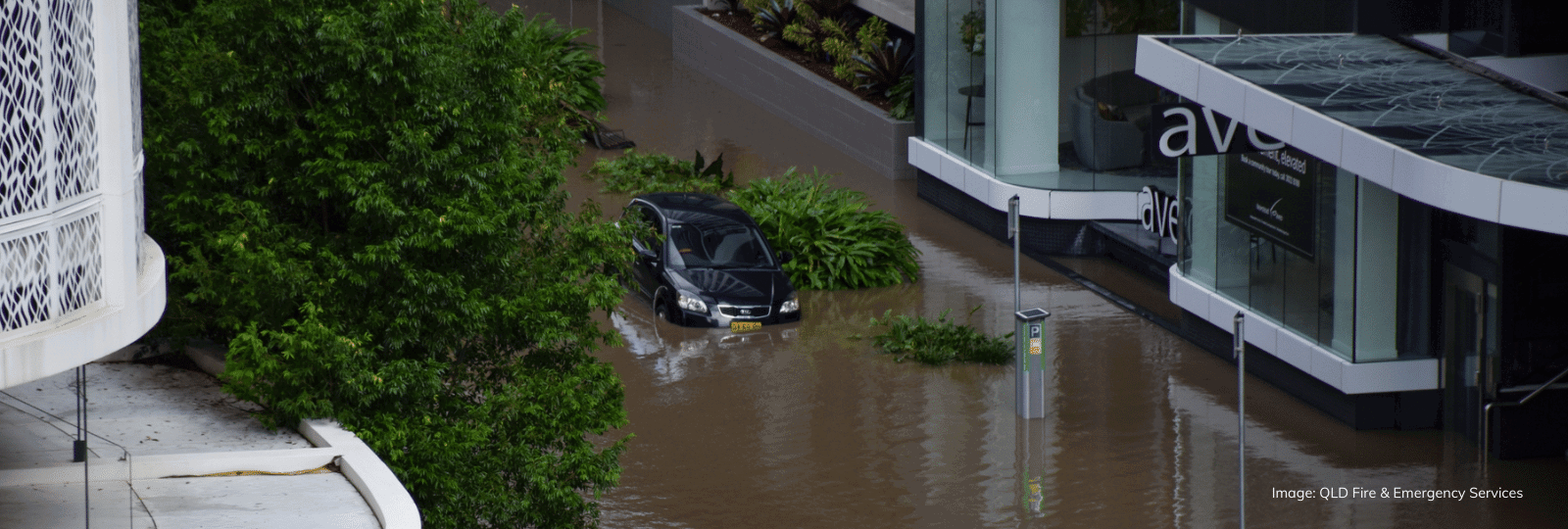 A flooded street, with a car with water up to its bonnet parked outside an apartment complex